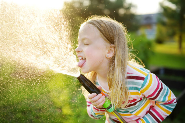 Adorable little girl playing with a garden hose on warm summer day. Child having fun with water on hot day. Outdoor summer activities for kids. - Fotografie, Obrázek