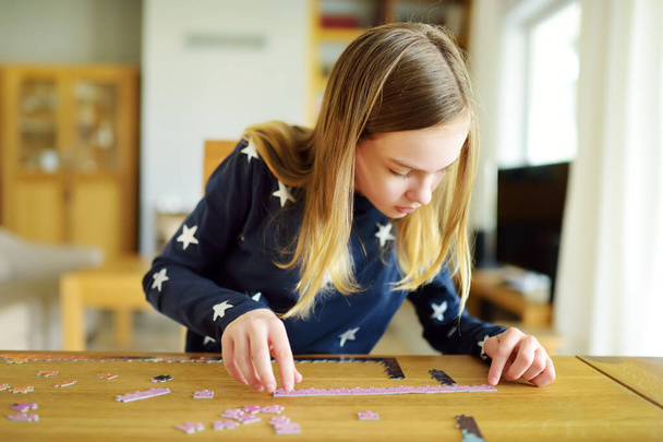 Cute young girl playing puzzles at home. Child connecting jigsaw puzzle pieces in a living room table. Kid assembling a jigsaw puzzle. Fun family leisure. Stay at home activity for kids. - Fotografie, Obrázek