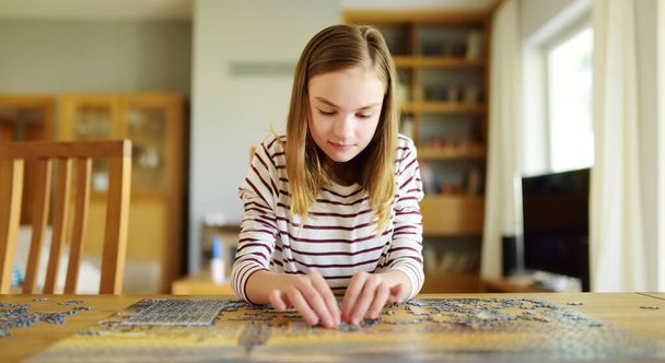 Cute young girl playing puzzles at home. Child connecting jigsaw puzzle pieces in a living room table. Kid assembling a jigsaw puzzle. Fun family leisure. Stay at home activity for kids. - Foto, Imagem