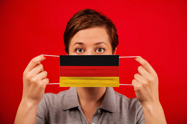 Coronavirus COVID-19 in Germany. Woman in medical protective mask with the image of the flag of Germany. The concept of preventing the spread of the epidemic and treating coronavirus. - Фото, зображення