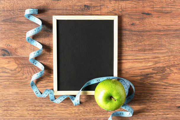 Green apple, measuring tape and chalkboard for text top view on wooden background. Diet planning concept. Copy space. - Foto, imagen