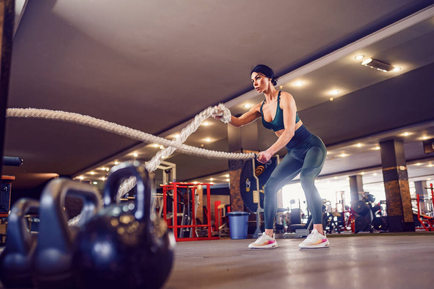 Кавказька жінка, одягнена в спортивний одяг, важко працює з бойовими мотузками в спортзалі. - Фото, зображення