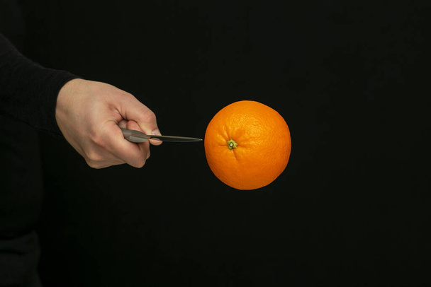 Mann schneidet im Flug eine Orange auf schwarzem Hintergrund - Foto, Bild