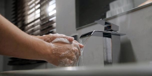 Zbliżenie kobiety stosującej mydło podczas mycia rąk w zlewie z otwartym kranem. Kobieta myje ręce mydłem nad umywalką w łazience. - Zdjęcie, obraz