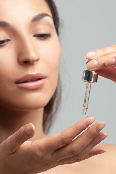 Young beautiful woman with clean perfect skin uses age-sensitive serum in pipette. Skin care and age cosmetics - Φωτογραφία, εικόνα