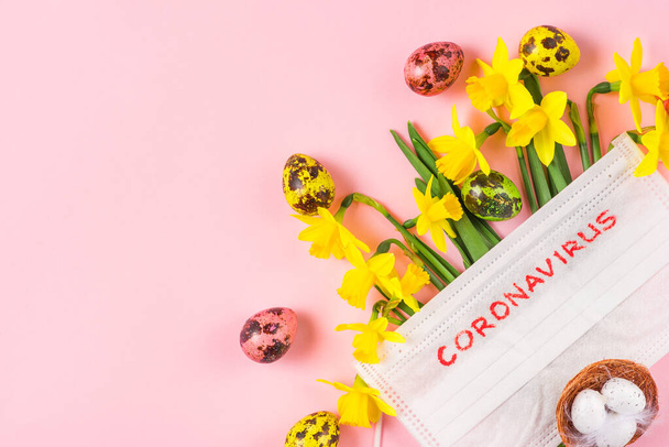 Coronavirus karantén a húsvéti ünnepek alatt. tavaszi nárcisz virágok arc orvosi maszk és tojás rózsaszín háttér. Lapos fekvés. felülnézet másolási hellyel - Fotó, kép