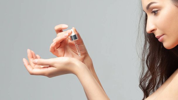 Young beautiful woman with clean perfect skin uses age-sensitive serum in pipette. Skin care and age cosmetics - 写真・画像