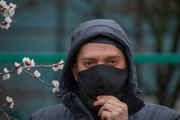 Een man met een zwart masker op zijn gezicht. Een man op straat met een zwart masker. Een virus. Coronavirus. Een man in de lente op straat met een masker om zich te beschermen tegen het infectievirus. - Foto, afbeelding