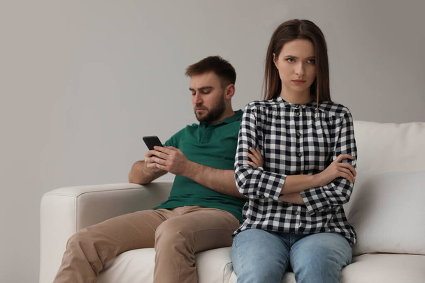 Young man preferring smartphone over his girlfriend at home. Relationship problems - 写真・画像