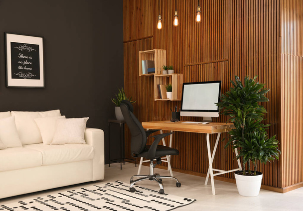 Comfortable workplace with computer near wooden wall in stylish room interior. Home office design - Foto, imagen