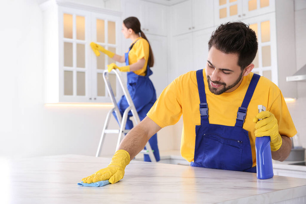 Professional young janitor cleaning table in kitchen - Foto, immagini