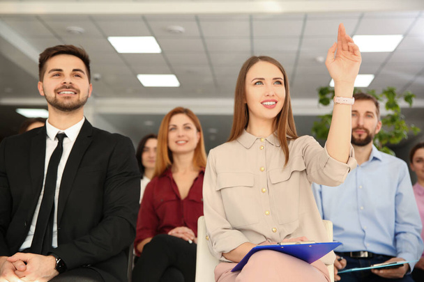 Young woman raising hand to ask question at business training indoors - Photo, Image