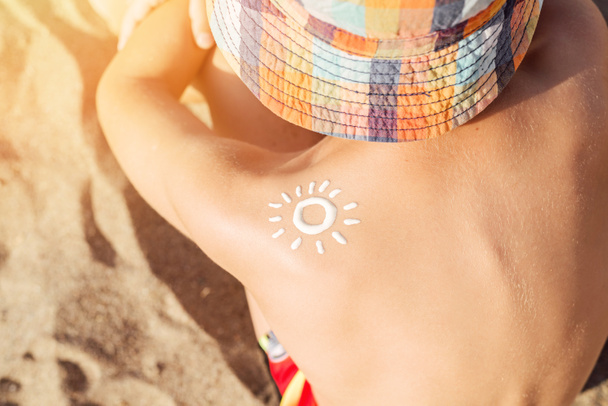 Zonnebrandcrème op de schouder van een gebruind kind, van dichtbij gezien. Zonwering op het strand. - Foto, afbeelding