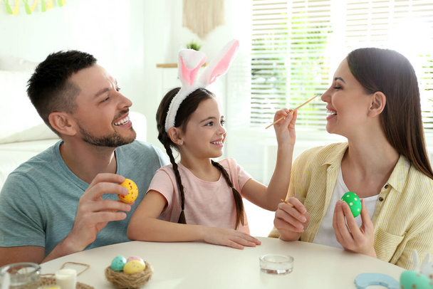 Happy father, mother and daughter having fun while painting Easter eggs at table indoors - Photo, image