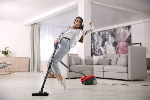 Young woman having fun while vacuuming at home - Foto, imagen