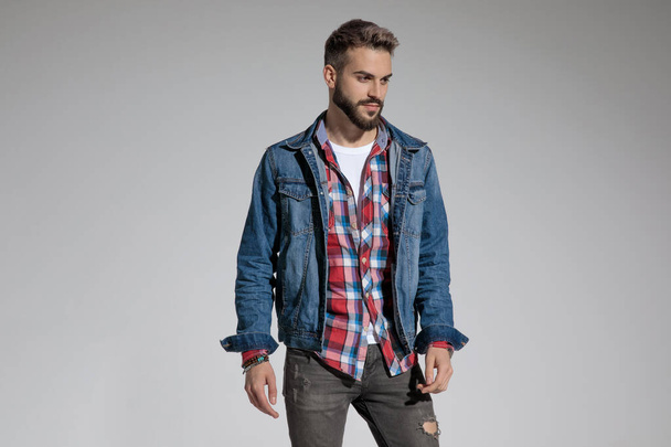 сексуальний випадковий чоловік у джинсовій куртці, що стоїть і позує зі стилем на сірому студійному фоні
 - Фото, зображення