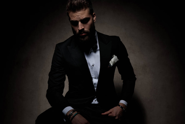 sexy uomo d'affari indossa nero smoking seduta e posa cool su sfondo scuro studio
 - Foto, immagini