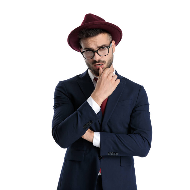 sexy podnikatel na sobě burgundský klobouk stojící a dotýkající se rty svůdný na bílém pozadí studia - Fotografie, Obrázek