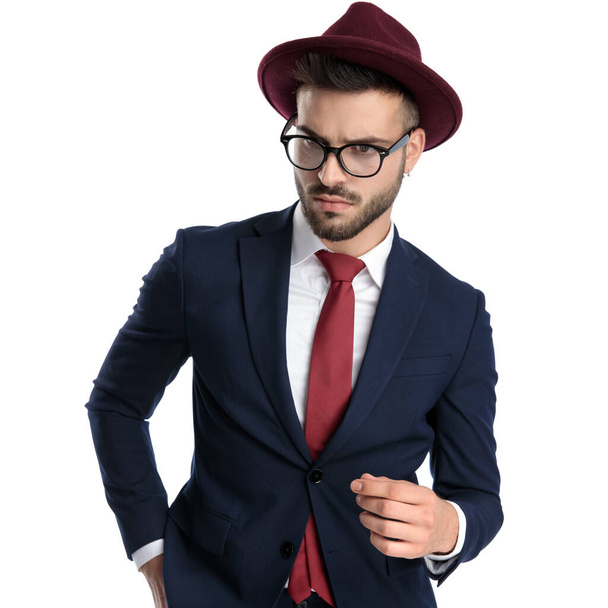 красивий бізнесмен в бордовому капелюсі стоїть з рукою в кишені і дивиться драматично на білому студійному фоні
 - Фото, зображення