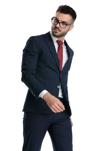 sexy formele man dragen bril lopen en kijken terug over schouder met koele houding op witte studio achtergrond - Foto, afbeelding