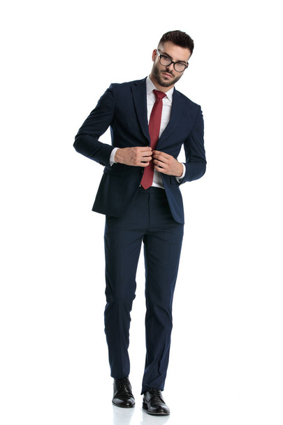 guapo hombre de negocios con gafas caminando mientras cierra su chaqueta seria sobre fondo de estudio blanco
 - Foto, imagen
