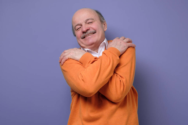 Piacere caucasico anziano uomo in maglione arancione si abbraccia, ha alta autostima sensazione felice di essere solo. Studio girato
 - Foto, immagini