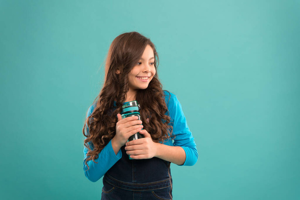 Living healthy life. Health and water balance. Girl hold water bottle blue background. Kid girl long hair has water bottle. Water balance concept. Strong and healthy child. Drink some liquids - Foto, imagen