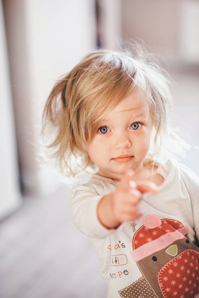 Babygirl with blonde hair and sky blue eyes pionts blurred finger - Foto, Imagen