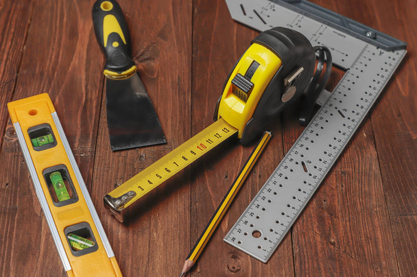 vista horizontal de un conjunto de herramientas de bricolaje en una mesa de madera, el conjunto incluye un flexómetro, lápiz, nivel de burbuja, carpintero cuadrado y una espátula
. - Foto, imagen