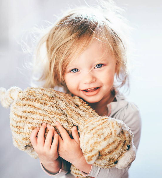 Gros plan d'une jolie blonde aux yeux bleus tenant un jouet en peluche dans sa main et souriant innocemment
 - Photo, image