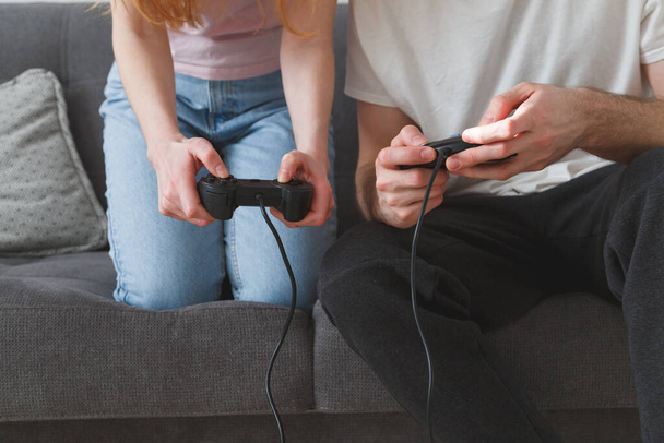 Egy fiatal pár, egy lány és egy srác joystickokkal a kezükben játszanak a konzolon, miközben a kanapén ülnek. - Fotó, kép