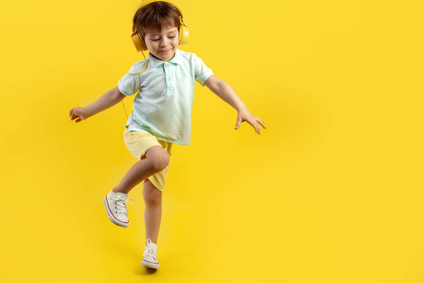 Full lengh photo of funny kid listening music in headphone and dance over yellow background. - Фото, изображение
