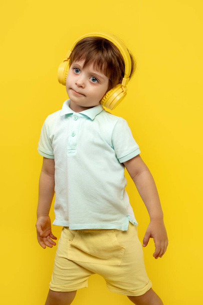 Charming kid listening music in headphone and dance over yellow background. - Foto, afbeelding
