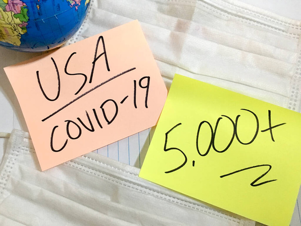USA Coronavirus COVID-19 infection medical cases and deaths United States. China COVID respiratory disease influenza virus statistics hand written on surgical mask and earth globe background - 写真・画像
