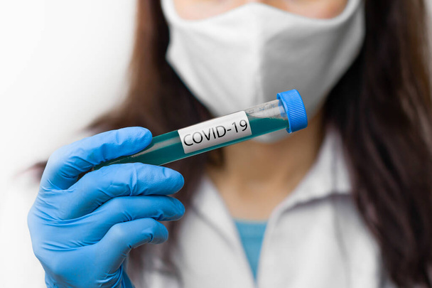 Koeputki, jossa on rokote koronavirusta vastaan, 2019-nCoV, SARS-nCov, COVID-19 tutkijan kädessä suojaava naamio ja siniset käsineet
 - Valokuva, kuva