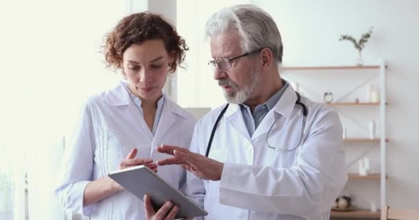 Experienced male senior physician holding digital tablet teaching female nurse - Felvétel, videó