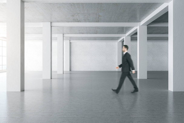 Businessman walking in concrete gallery interior with empty wall and columns. Mock up, - Foto, Imagen