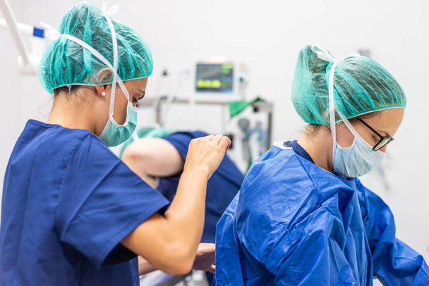 Medical assistant helping a surgeon put on sterile clothes in an operating room. - Fotó, kép