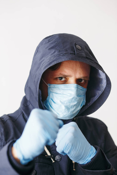 Boks pozisyonunda Coronavirus 'tan korumak için maskeli bir adam. Corona virüsü salgını. Tıbbi maskeli genç adam izole edildi. Kapüşonlu, tıbbi maskeli biri. COVID-19 - Fotoğraf, Görsel