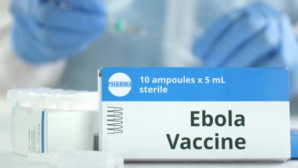 Ampullen mit Ebola-Impfstoff auf dem Tisch in der Nähe der arbeitenden Laborantin, fiktives Logo auf der Verpackung - Filmmaterial, Video