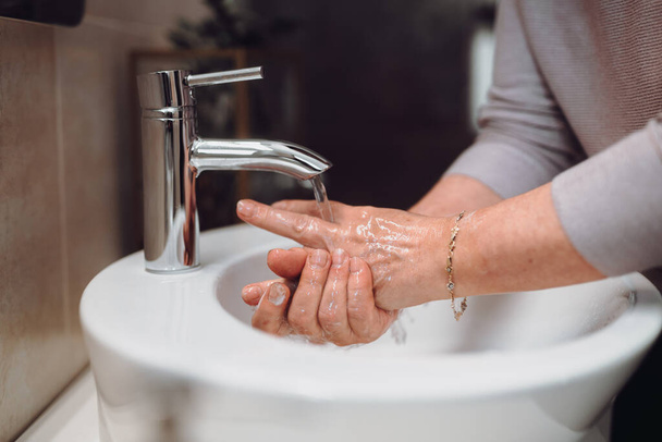 Dünya çapında koronavirüs salgını sırasında evde ellerini sabun ve dezenfektanla dikkatlice yıkayan bir kadın. - Fotoğraf, Görsel
