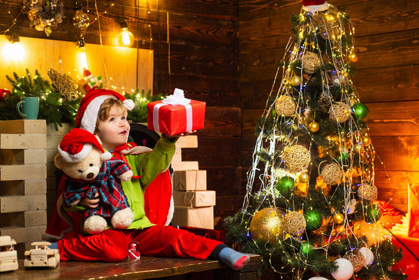 Oyuncak ayısıyla ve Noel hediyesiyle küçük mutlu çocuk hediyesinin içinde ne olduğunu tahmin etmeye çalışıyor. Kış, tatil, aile zamanı.. - Fotoğraf, Görsel
