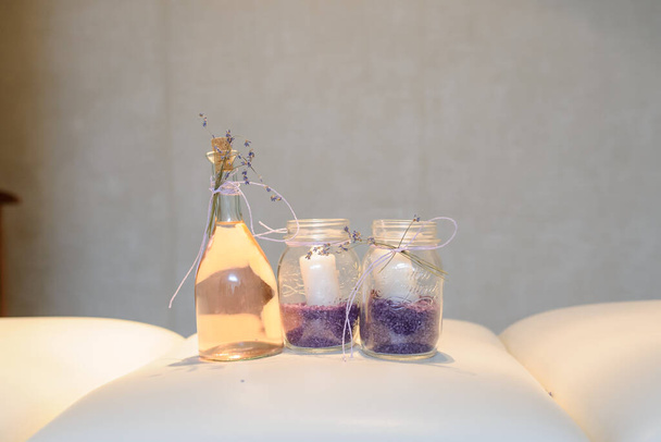 boczny widok butelki vintage z olejkiem do masażu i 2 szklanki ze świecami i solą do kąpieli lavanda na łóżku do masażu - Zdjęcie, obraz