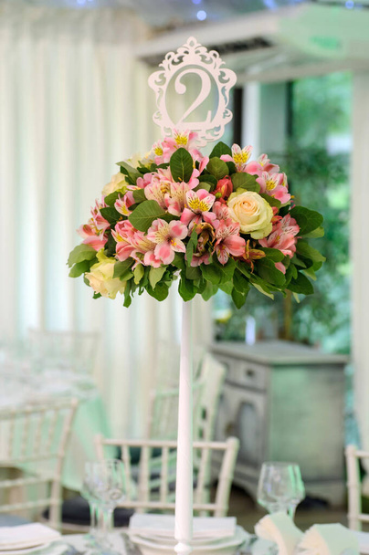 Svatební presidiový stůl s bílým a šedým ubrusem, květinové aranžmá: kytice o květ v bílé váze, svíčky ve stříbrné podpěře, bílé křeslo na pozadí - Fotografie, Obrázek