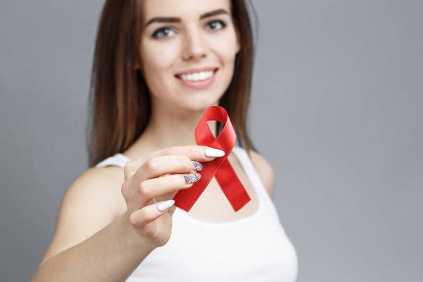 Mãos femininas segurando fita vermelha da consciência da AIDS
 - Foto, Imagem