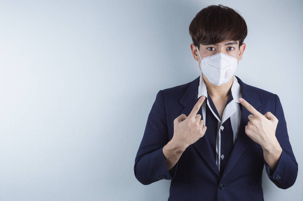 De zakenman met het gezichtsmasker tegen het coronavirus, PM 2.5 en kou, en zijn vingerwijzer op zijn masker. - Foto, afbeelding