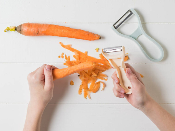 Lapsi puhdistaa ja viipaloi porkkanoita erityisillä veitsillä puupöydällä
. - Valokuva, kuva