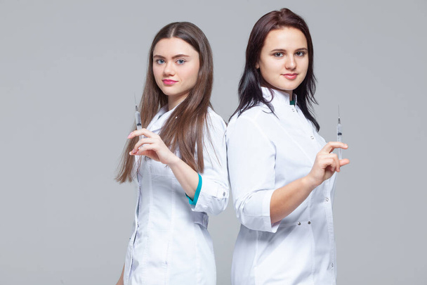 Two female doctors standing back-to-back hold ready-to-inject syringes - Fotó, kép