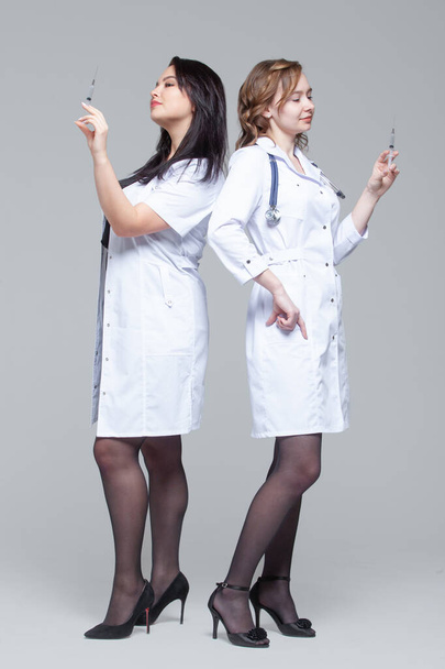 Full-length portrait of two female doctors standing back-to-back hold ready-to-inject syringes - Foto, Imagem