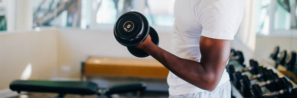 Young African American man standing and lifting a dumbbell with the rack at gym - Φωτογραφία, εικόνα
